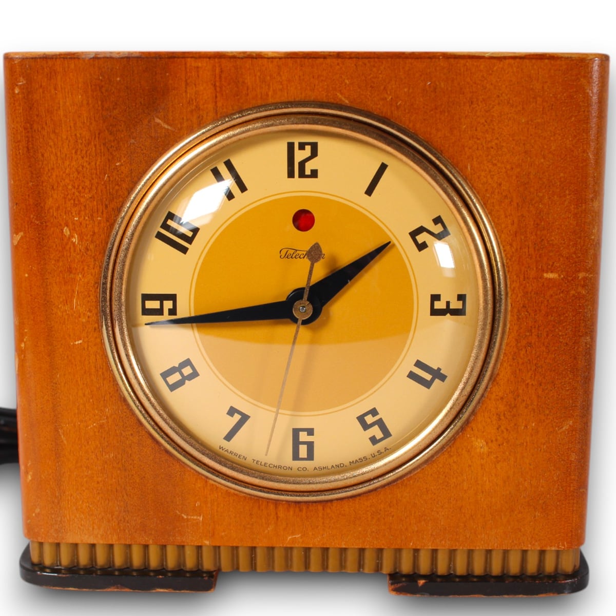 Archived catalog photograph of a square wood-toned Telechron clock with a round yellow dial, dark geometric numerals, and fluted base trim