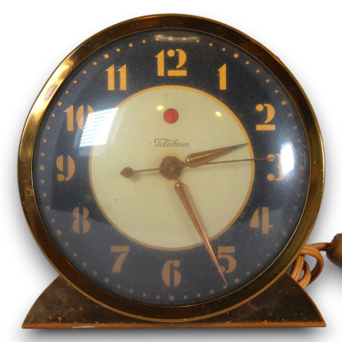 Archived catalog photograph of a round Telechron easel clock with a black dial ring, cream center, brass-toned numerals, and triangular base