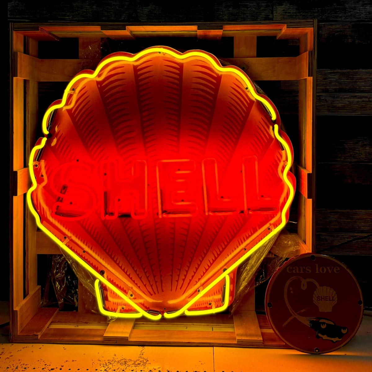 Archived catalog photograph of an illuminated shell-shaped red and yellow display supported inside a wood shipping frame