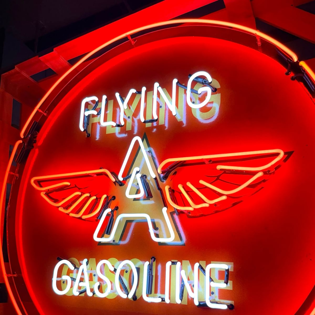 Archived catalog photograph of an illuminated round red display with formed-glass tubing spelling Flying A Gasoline around a winged letter A