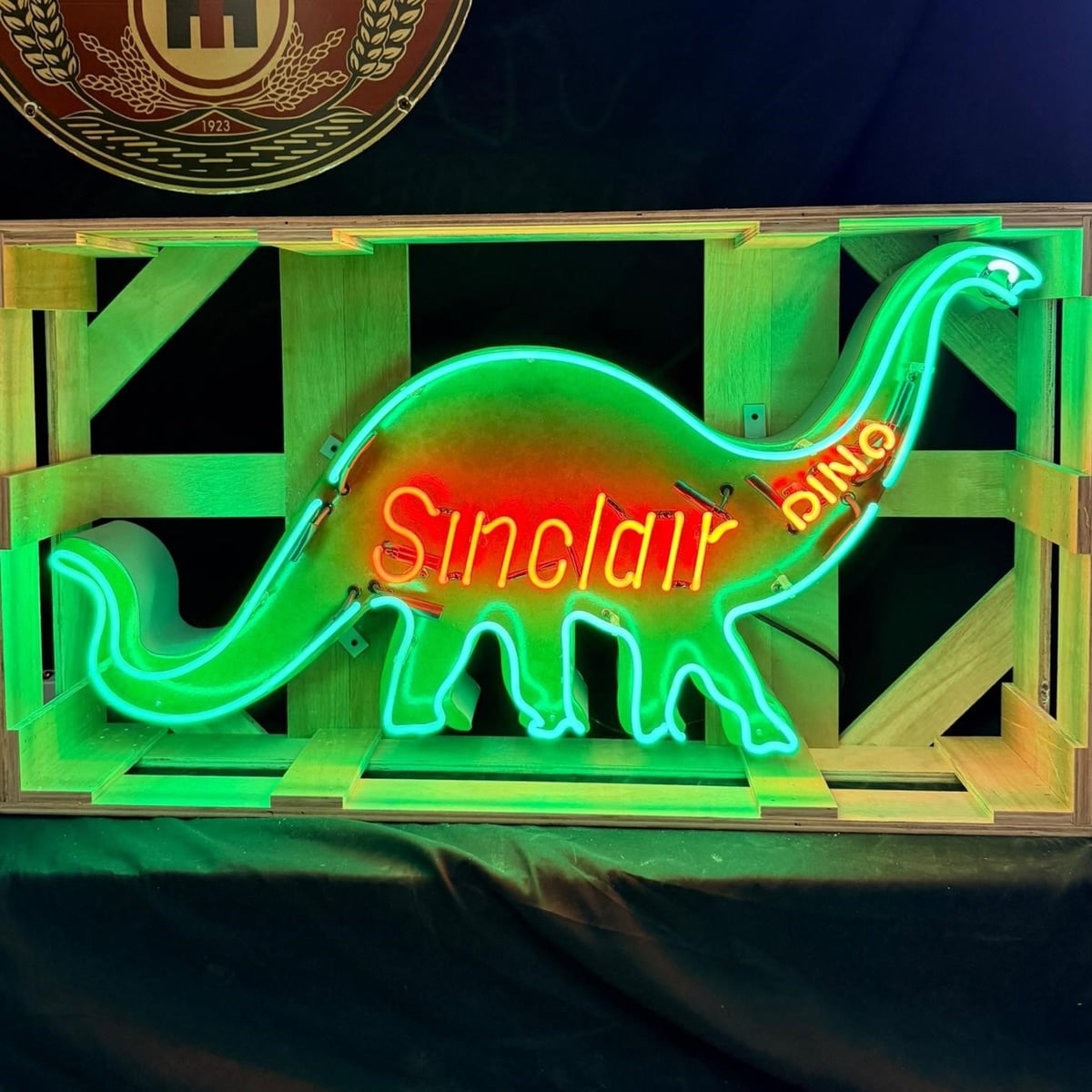Actual catalog photograph of an illuminated green Sinclair dinosaur-shaped neon display with red Sinclair lettering, mounted in a wood shipping frame