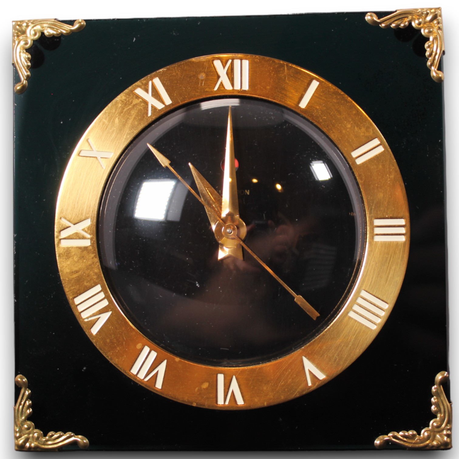 Catalog photograph of a square black tabletop clock with gold-toned numerals and corner decoration